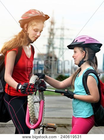 Bicycle tire pumping by child bicyclist. Girl wearing bicycle helmet with hand pump. Kids pump up tire. There are road and traffic sign at background. Children return home from school on bicycles.