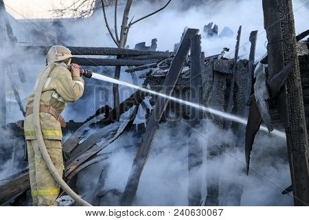 Firefighter Extinguishes The Fire. Fireman Holding A Hose With Water, Watering A Strong Stream Of Bu