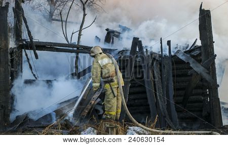 Firefighter Extinguishes The Fire. Fireman Holding A Hose With Water, Watering A Strong Stream Of Bu