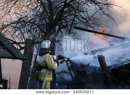 Firefighter Extinguishes The Fire. Fireman Holding A Hose With Water, Watering A Strong Stream Of Bu