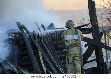Firefighter Extinguishes The Fire. Fireman Holding A Hose With Water, Watering A Strong Stream Of Bu