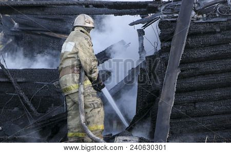 Firefighter Extinguishes The Fire. Fireman Holding A Hose With Water, Watering A Strong Stream Of Bu
