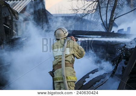 Firefighter Extinguishes The Fire. Fireman Holding A Hose With Water, Watering A Strong Stream Of Bu