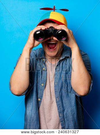 Young Nerd Man With Noob Hat Using A Binoculars On Blue Background