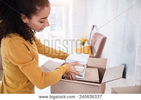 Necessary Books. Charming Curly-haired Girl Fitting A Pile Of Books Into The Box While Preparing To 