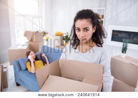 Mad At You. Curly-haired Young Girl Looking At The Camera With Annoyed Expression And Carrying A Hea