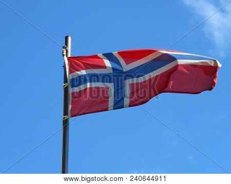 National Flag Of Norway On A Flagpole In Front Of Blue Sky.
