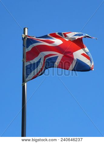 National Flag Of United Kingdom On A Flagpole In Front Of Blue Sky.