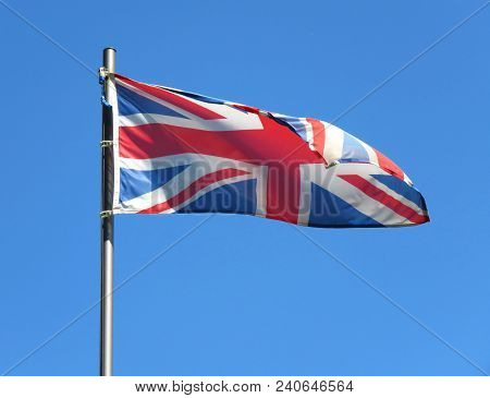 National Flag Of United Kingdom On A Flagpole In Front Of Blue Sky.