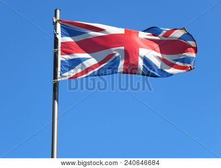 National Flag Of United Kingdom On A Flagpole In Front Of Blue Sky.