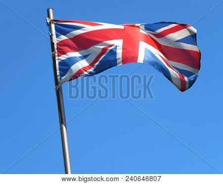 National Flag Of United Kingdom On A Flagpole In Front Of Blue Sky.