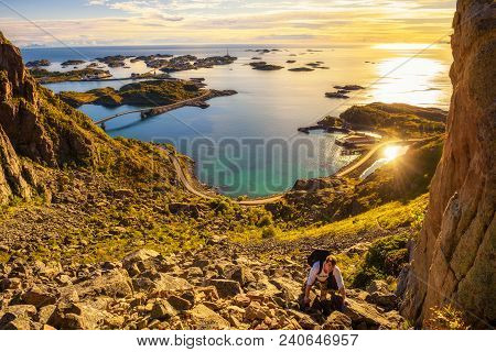 Young Hiker Going To The Top Of Mount Festvagtinden With Views Over The Village Of Henningsvaer On L