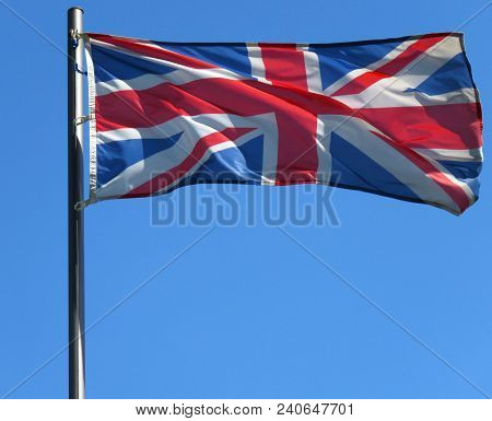 National Flag Of United Kingdom On A Flagpole In Front Of Blue Sky.