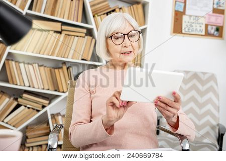 Educational Courses. Musing Senior Woman Using Tablet While Sitting In Chair