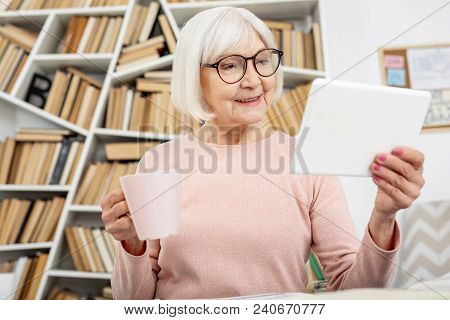 New Facts. Enthusiastic Senior Woman Using Tablet While Enjoying Tea