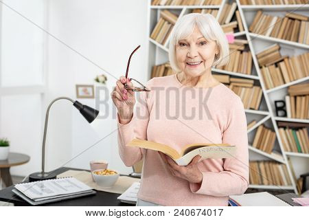 Informative Book. Joyful Mature Woman Holding Glasses And Reading Book