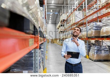 logistic business, shipment and people concept - happy businessman with clipboard at warehouse