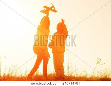Two little sisters holding hands and playing with small airplane toy outdoors. Silhouette of two sisters walking on the meadow at sunset