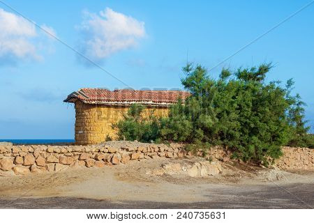 Abandoned Building Built Of Stone Bricks And Red Tiled Roof, Short Green Tree And Stone Fence On Bac