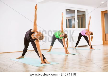 Three Girls Practicing Yoga, Trikonasana / Bikram Triangle Left Pose