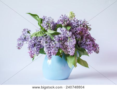 Beautiful Bouquet Of Fragrant Purple Flowers In Blue Ceramics Vase On Light Background. Syringa Vulg