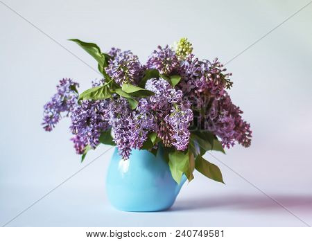 Beautiful Bouquet Of Fragrant Purple Flowers In Blue Ceramics Vase On Light Background. Syringa Vulg