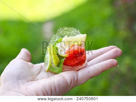 Melting Ice Cube With Strawberry, Lemon And Fresh Green Mint Leaves In A Hand