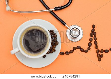 White Cup Of Coffee On Saucer With Coffee Beans Folded In The Form Of A Cardiogram And Phonendoscope