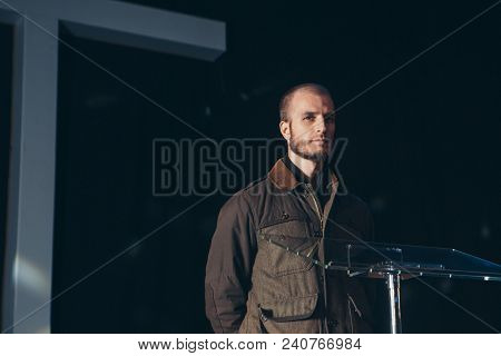 Man At The Pulpit Against The White Cross. Blonde In Jacket Of Preaching In The Church