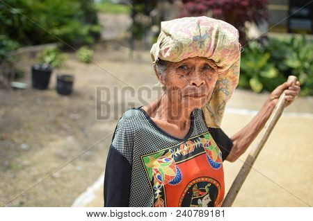 Sumatra, Indonesia - January 15, 2018: Elderly Farmer Looks Into The Camera Which Sun Drying Rice In