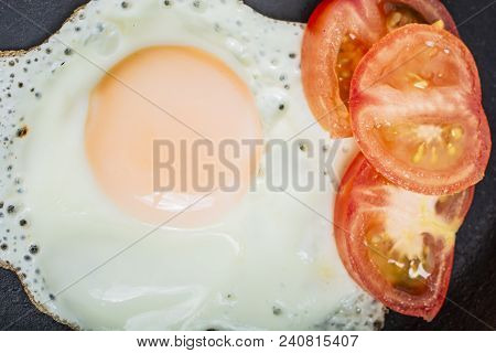 Fried Egg Fried With Chopped Tomatoes In A Cast-iron Frying Pan On A Wooden Table