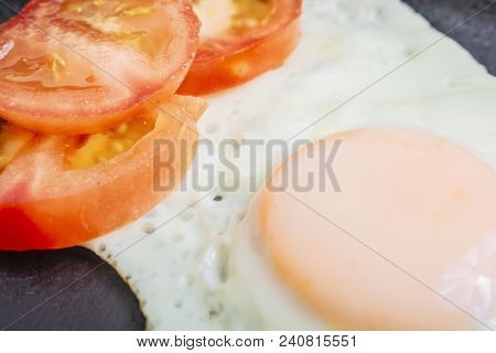 Fried Egg Fried With Chopped Tomatoes In A Cast-iron Frying Pan On A Wooden Table