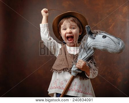 Cute Little Girl Dressed Like A Cowboy Playing With A Homemade Horse. Expressive Facial Expressions.
