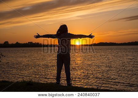 A Child In The Shade Of A Red Sunset, Is Spreading His Hands To The Sun