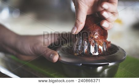 A Hand Squeezing Juice From A Red Orange On A Manual Glass Squeezer. Kitchen Background. Side View.