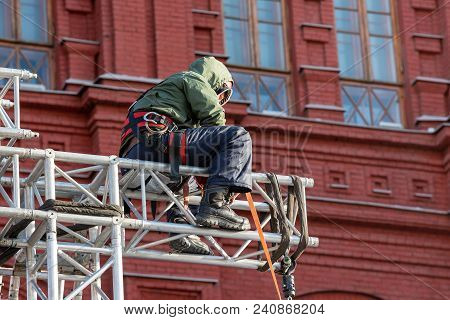 Industrial Climber In Uniform Sitting On A Building Structure. Alpinist Worker Checks His Equipment
