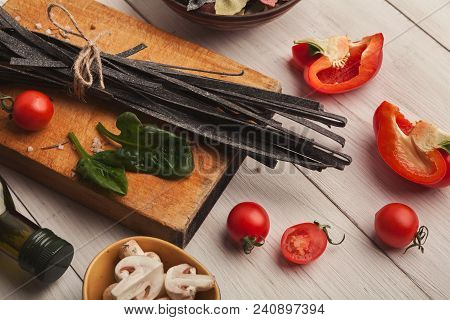 Cooking Pasta Background. Black Colored Fettuccine With Cuttle Fish Ink, Vegetables And Spices On Wh