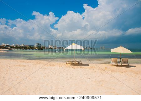 Sun Loungers And A White Umbrellas For Tourists On The Beach In Cancun. Mexico.