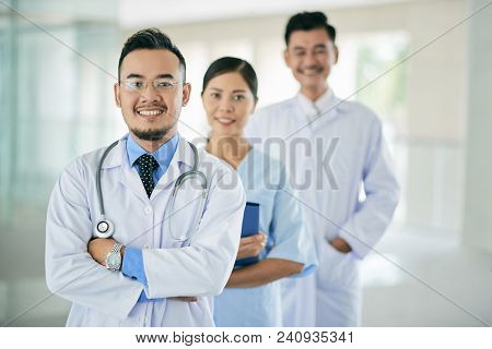 Cheerful Vietnamse General Practitioner And His Coworkers Standing Behind