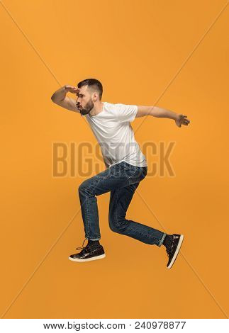 Freedom In Moving. Mid-air Shot Of Handsome Happy Young Man Jumping And Gesturing Against Orange Stu
