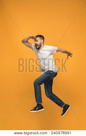 Freedom In Moving. Mid-air Shot Of Handsome Happy Young Man Jumping And Gesturing Against Orange Stu