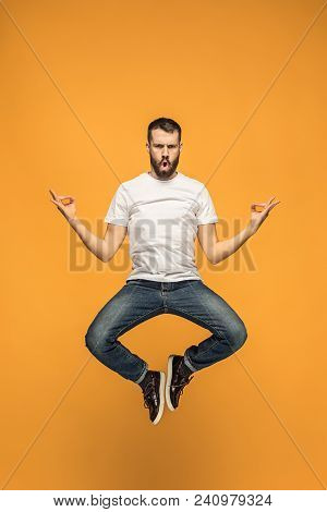 Freedom In Moving. Mid-air Shot Of Handsome Happy Young Man Jumping And Gesturing Against Orange Stu