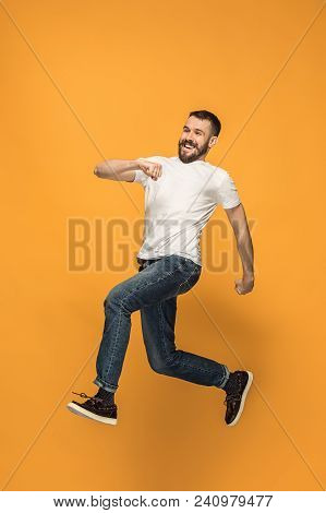 Freedom In Moving. Mid-air Shot Of Handsome Happy Young Man Jumping And Gesturing Against Orange Stu