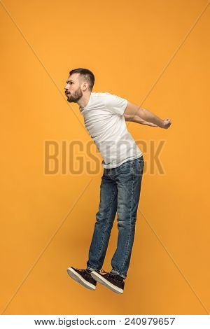 Freedom In Moving. Mid-air Shot Of Handsome Happy Young Man Jumping And Gesturing Against Orange Stu