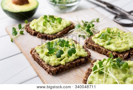 Healthy Nutrition. Fresh Wholegrain Toasts With Avocado And Microgreens On Kitchen Table, Close Up