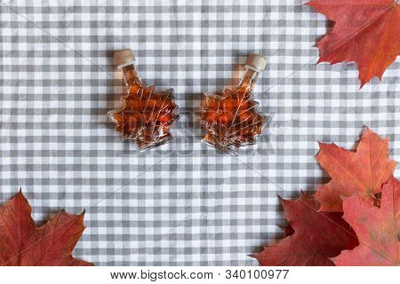 Maple Syrup In A Bottle In A Shape Of Maple Leaf. Red Maple Leaf Background.