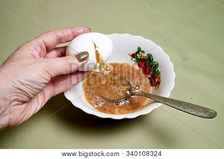 Raw Egg On A White Plate The Table, Small Spices In It And A Spoon In A Womans Handon. Cooking Eggs 