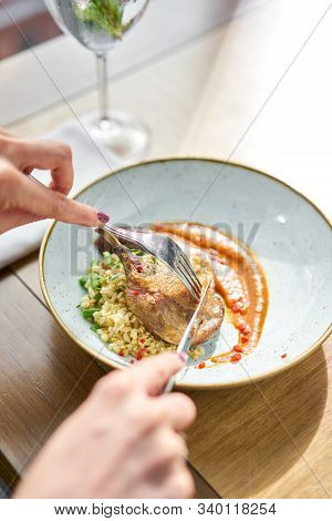 Lunch In A Restaurant, A Woman Cuts Delicious Duck Leg Su-vide, With Bulgur And Onion Marmalade. Bar