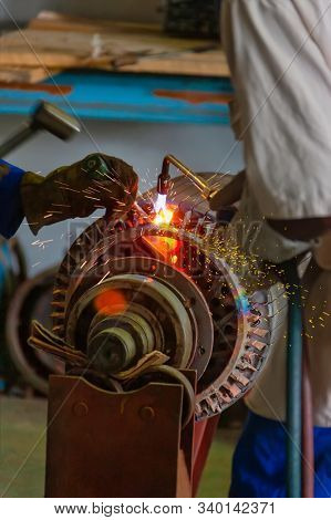 African man with a torch heating a rotor of an opened case motor , rewinding a giant electric motor