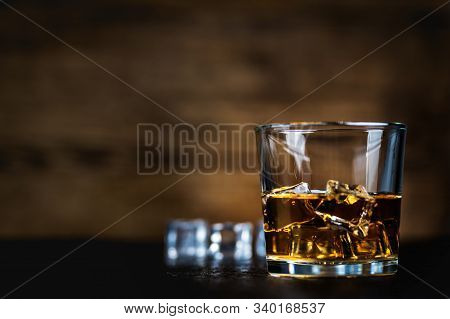 Whisky, Whiskey, Bourbon Or Cognac With Ice Cudes On Black Stone Table And Wood Background
